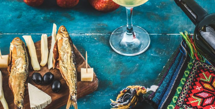 Cheese sticks with smoked fish on blue background with a glass of wine